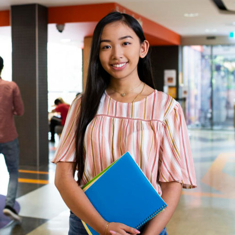 female standing in hallway with blue folder.