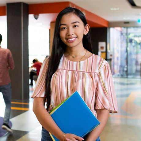 female standing in hallway with blue folder.
